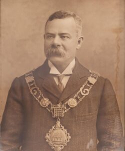 a portrait of Allan Glaisyer Minns Britain's first black Mayor, wearing Mayoral chains with the Thetford Town Council Crest